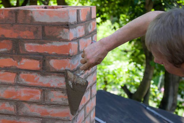 Trowel striking fresh mortar joints on a brick chimney